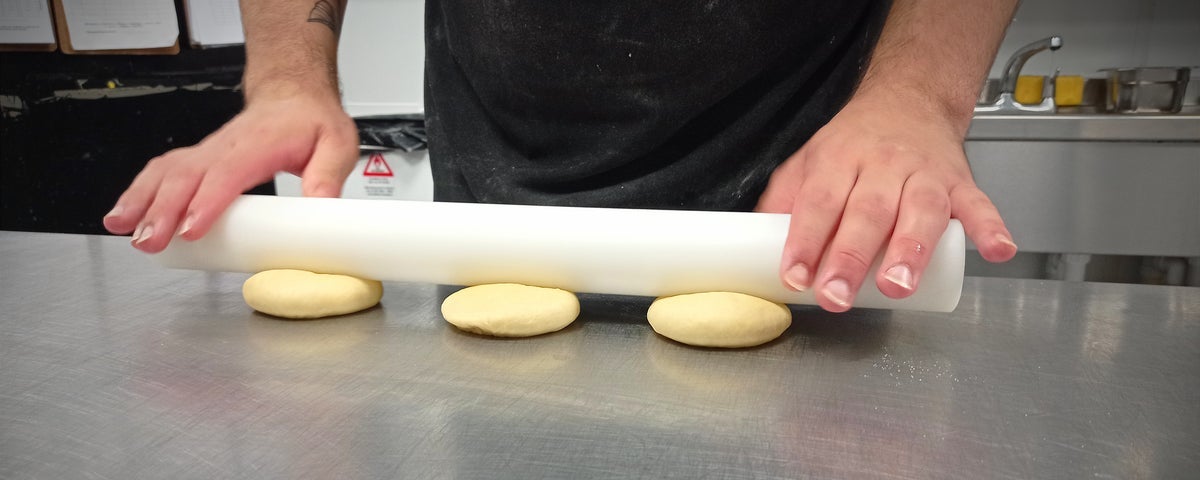 A person rolling three small slabs of dough with a rolling pin
