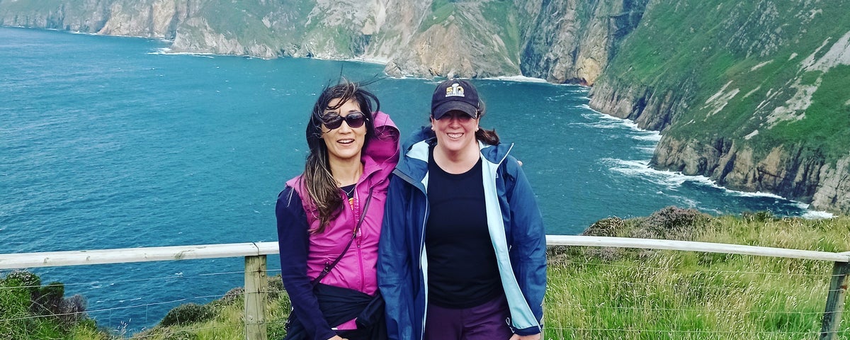 Two ladies standing on a platform with the sea and cliffs behind them