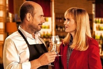 A man and woman standing close looking at each other, clinking glasses of wine together.