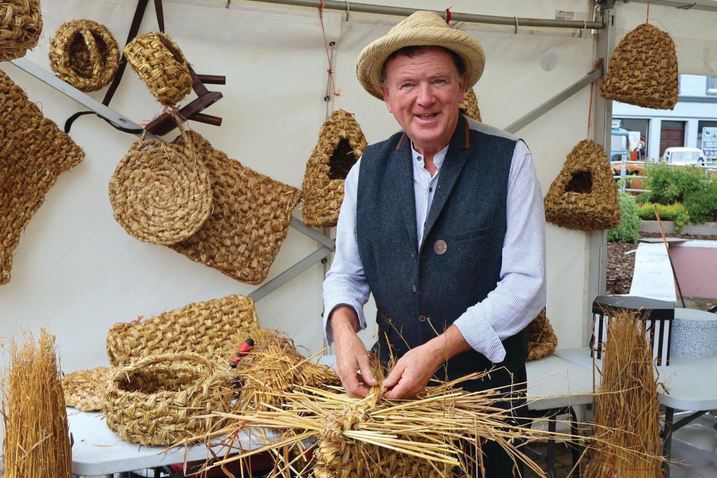 Image of Mr Padraig Larkin - a smiling man with items woven from straw on display.