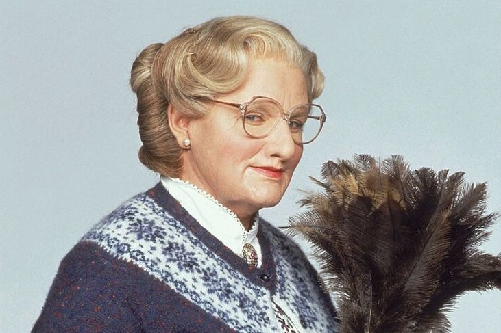 A older woman holding a feather duster looking slightly smug