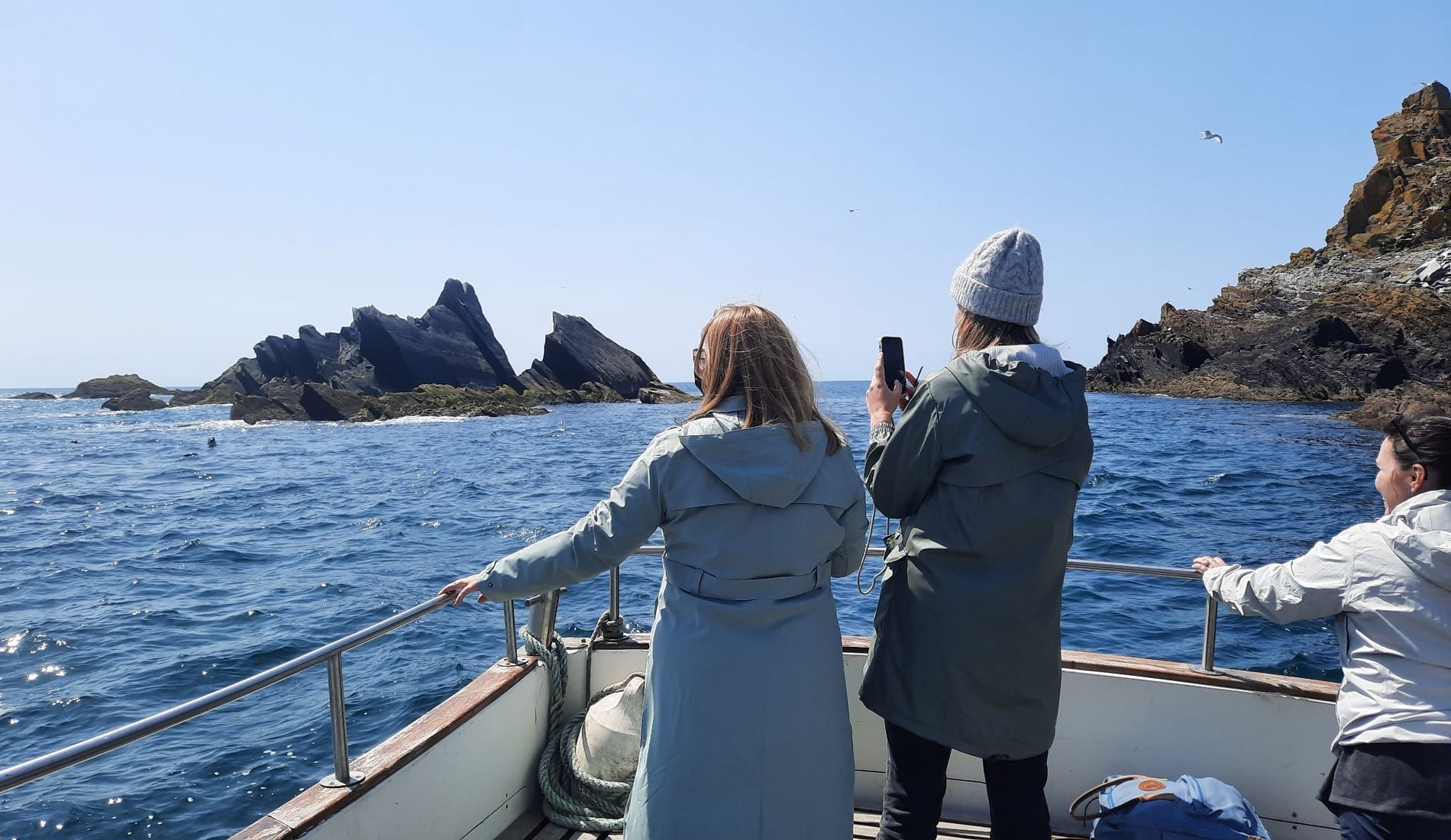 People on a boat tour viewing rocky coastal cliffs on a sunny day