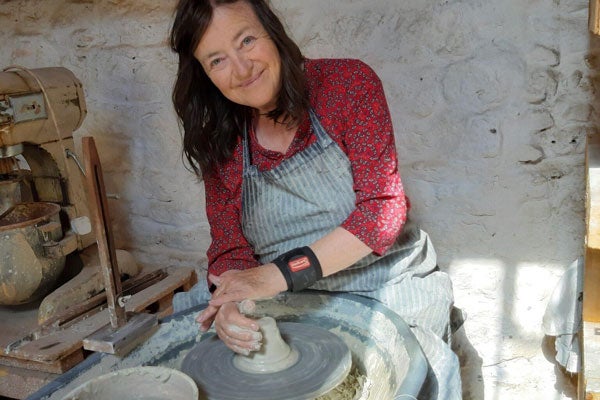 A lady at a pottery wheel smiling at the camera