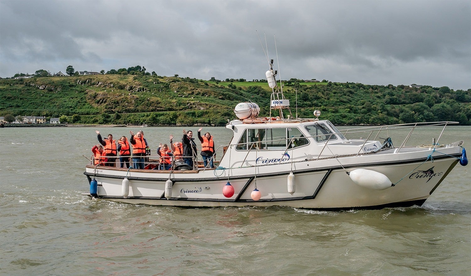A group of people wearing orange life vests on a boat called the Orinoco