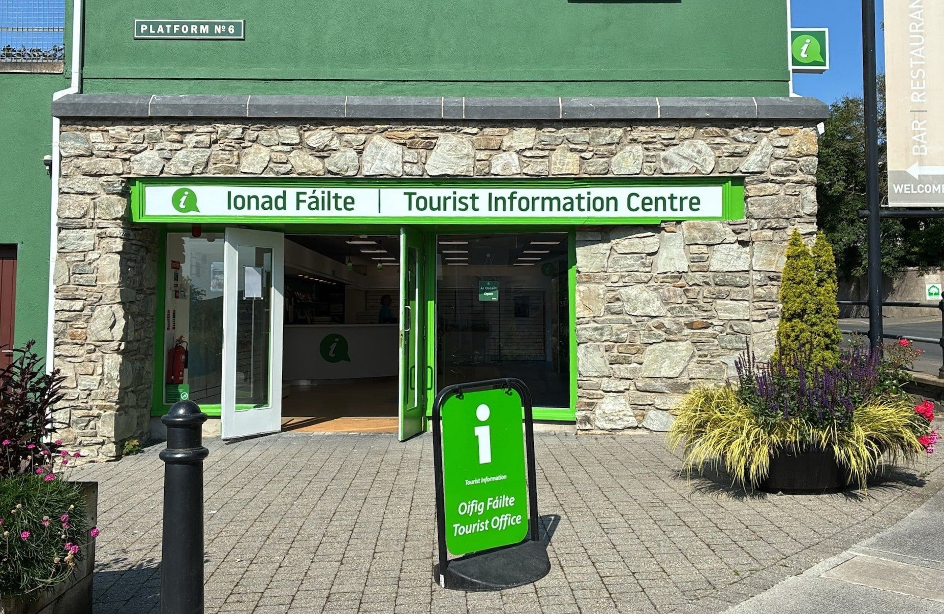 A stone clad shopfront with green and white signage for Clifden Tourist Information Centre