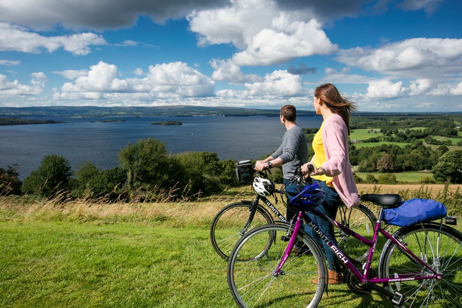 Two cyclists standing with their bikes looking out onto a lake