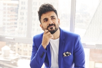 A man in blue suit with chin resting on right hand, looking thoughful, sitting on a window ledge.