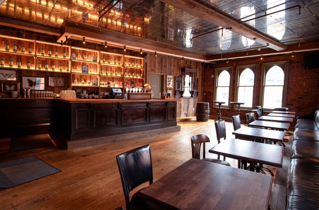 Interior of a pub with lots of wooden tables, flooring and bar along with old style windows
