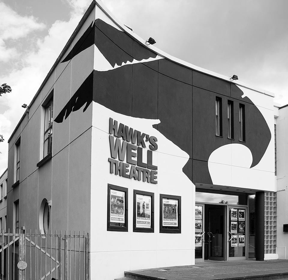 Black and white image of exterior of a theatre with three posters on the wall and railings to the left