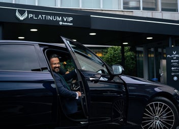 A person sits in the drivers seat of a car with the door open outside a building