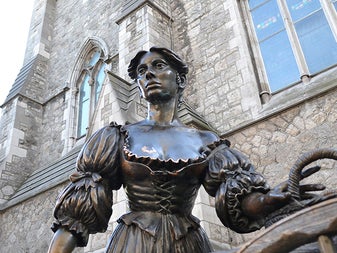 A statue of a woman in period dress on a city street