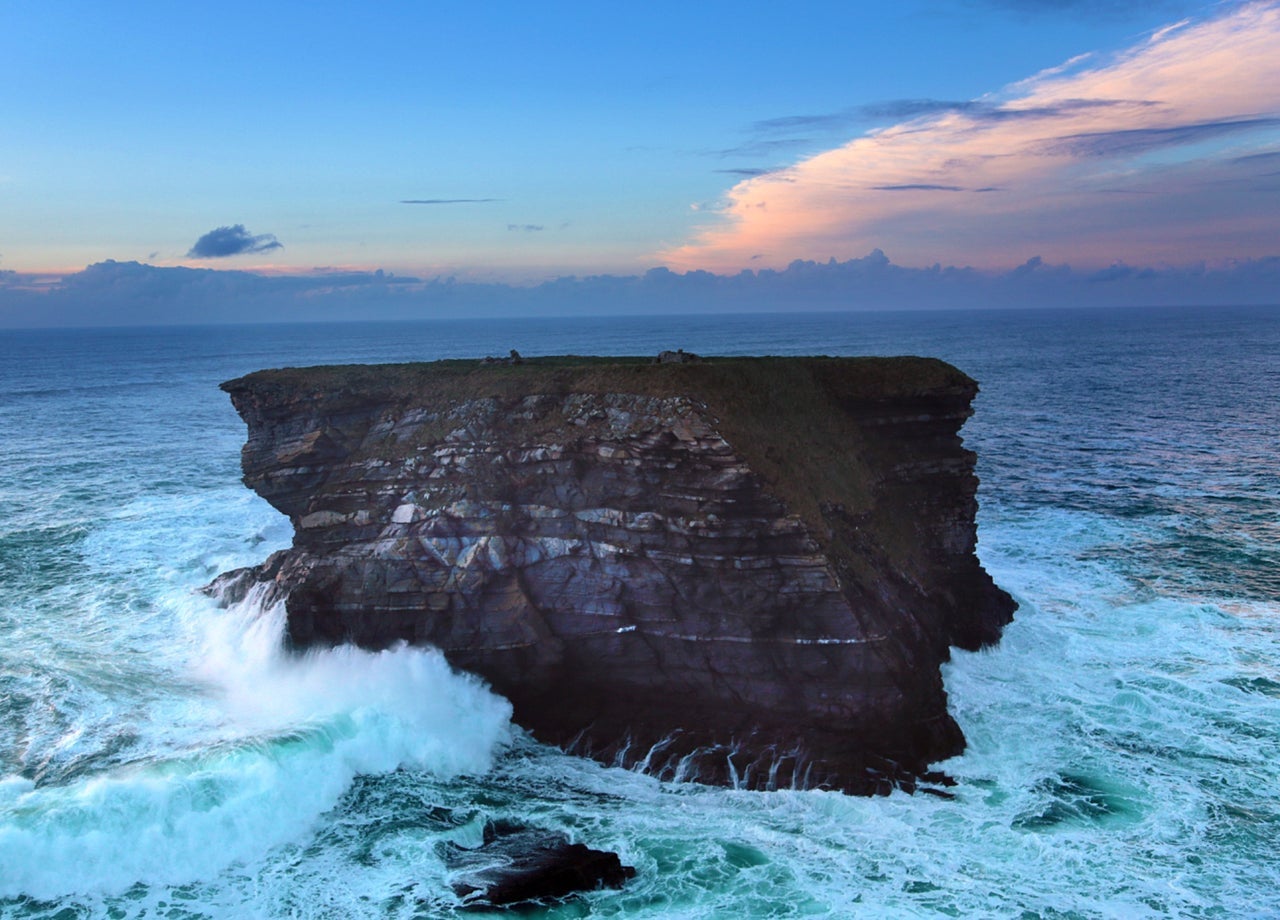 Waves crashing on a sea stack with the sun setting in the background