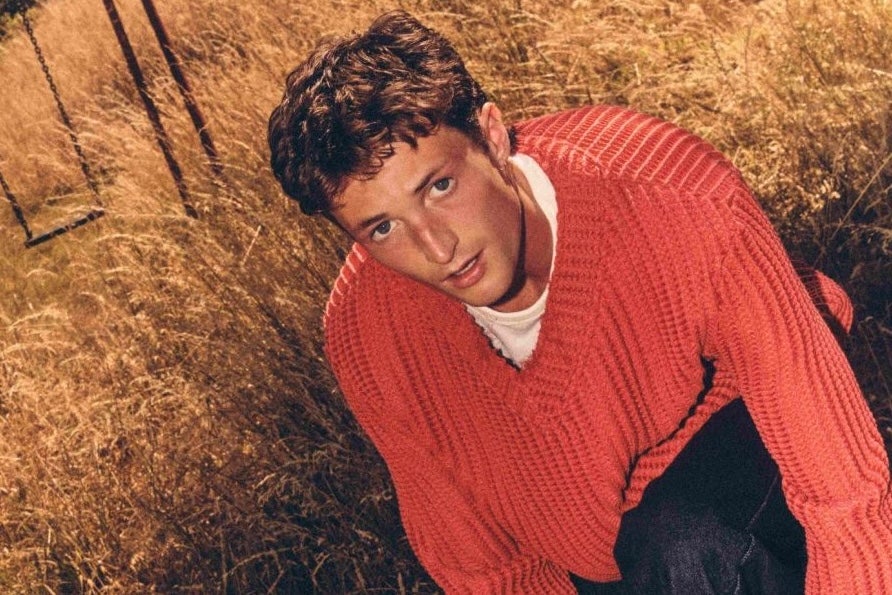 A young man in orange jumper in a field of brown long grass