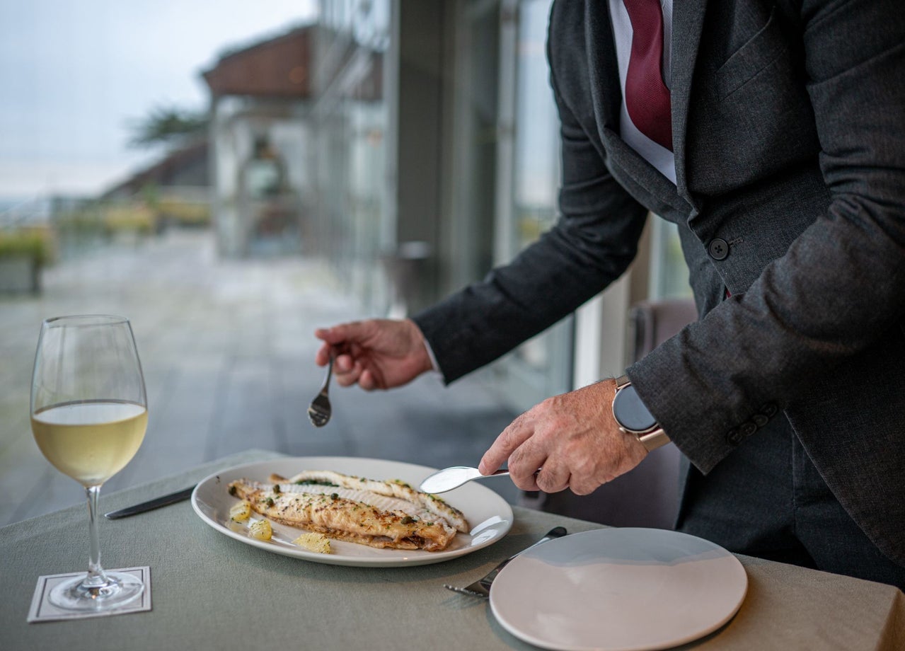 A fillet of grilled fish is being served with a glass of white wine