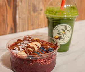 A close up of a bowl with seeds and fruit and a plastic smoothie cup with a business logo