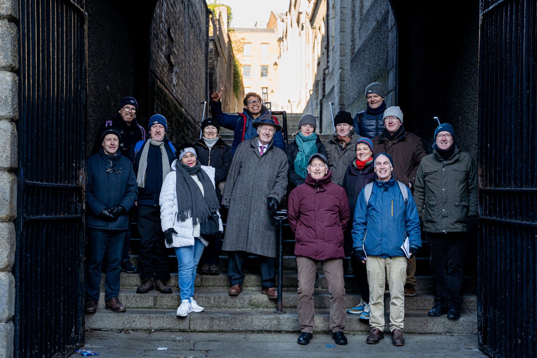 A guided walking tour group gathered on stone steps beneath an old iron gateway in Dublin, wrapped up against the cold as they explore the city's dark and storied past.