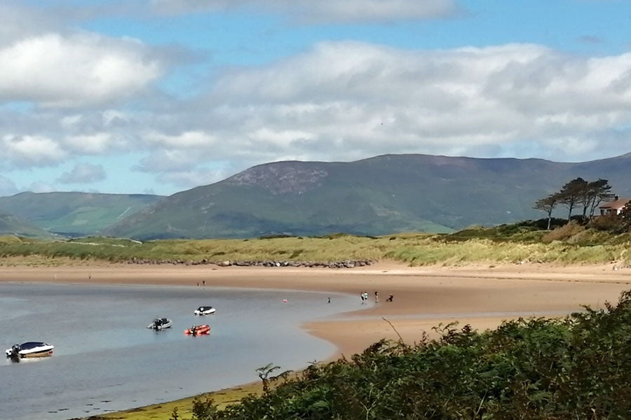 A view of the sandy Dooks Beach with some boats in the water and people walking on the beach