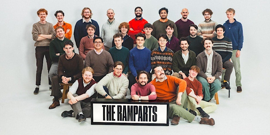 A large group of smiling men, some seated, the rest standing, against plain white background.