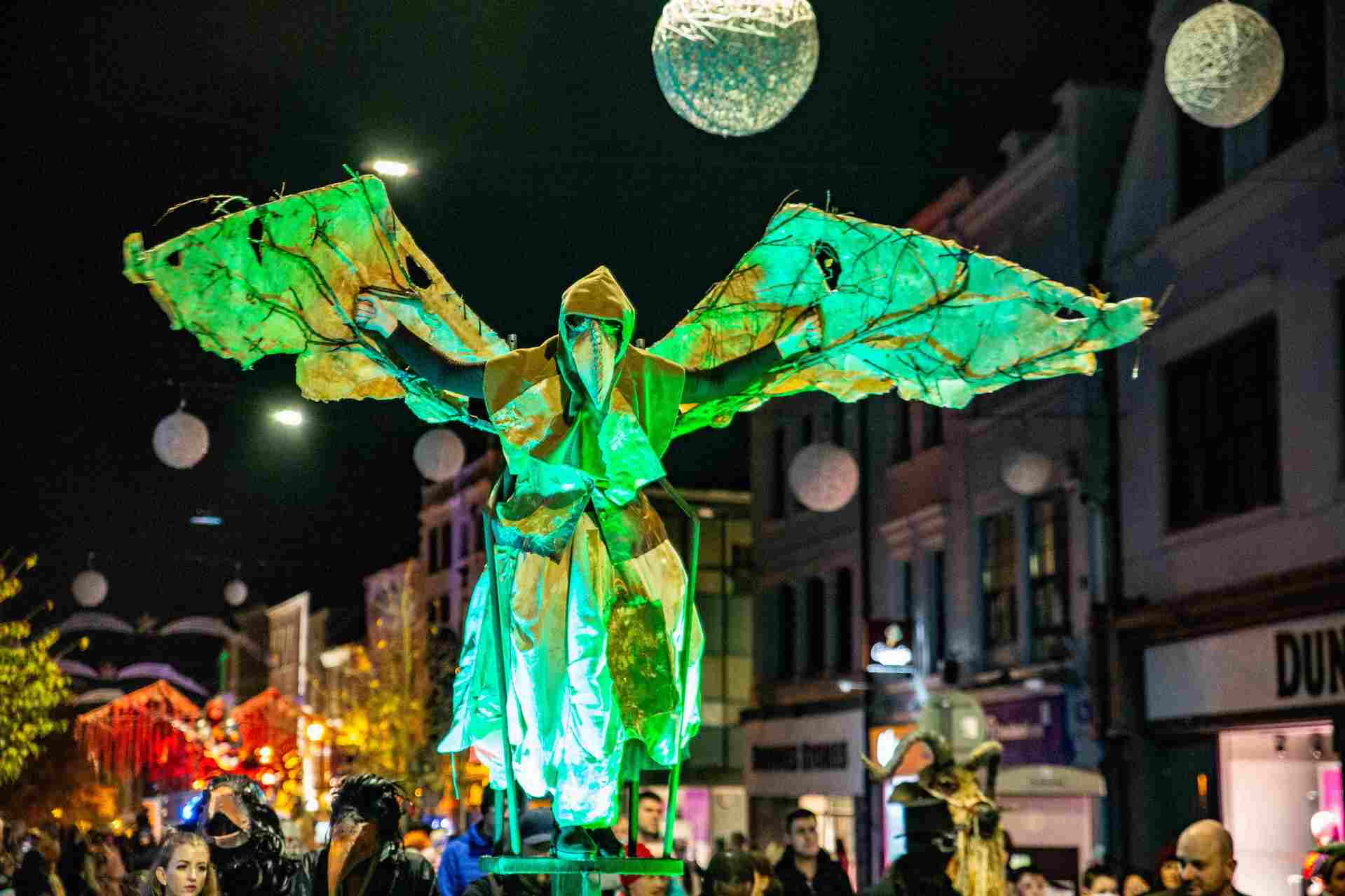 Samhain with Waterford Spraoi. At night in a street parade, a large, green winged costume is above the crowd.