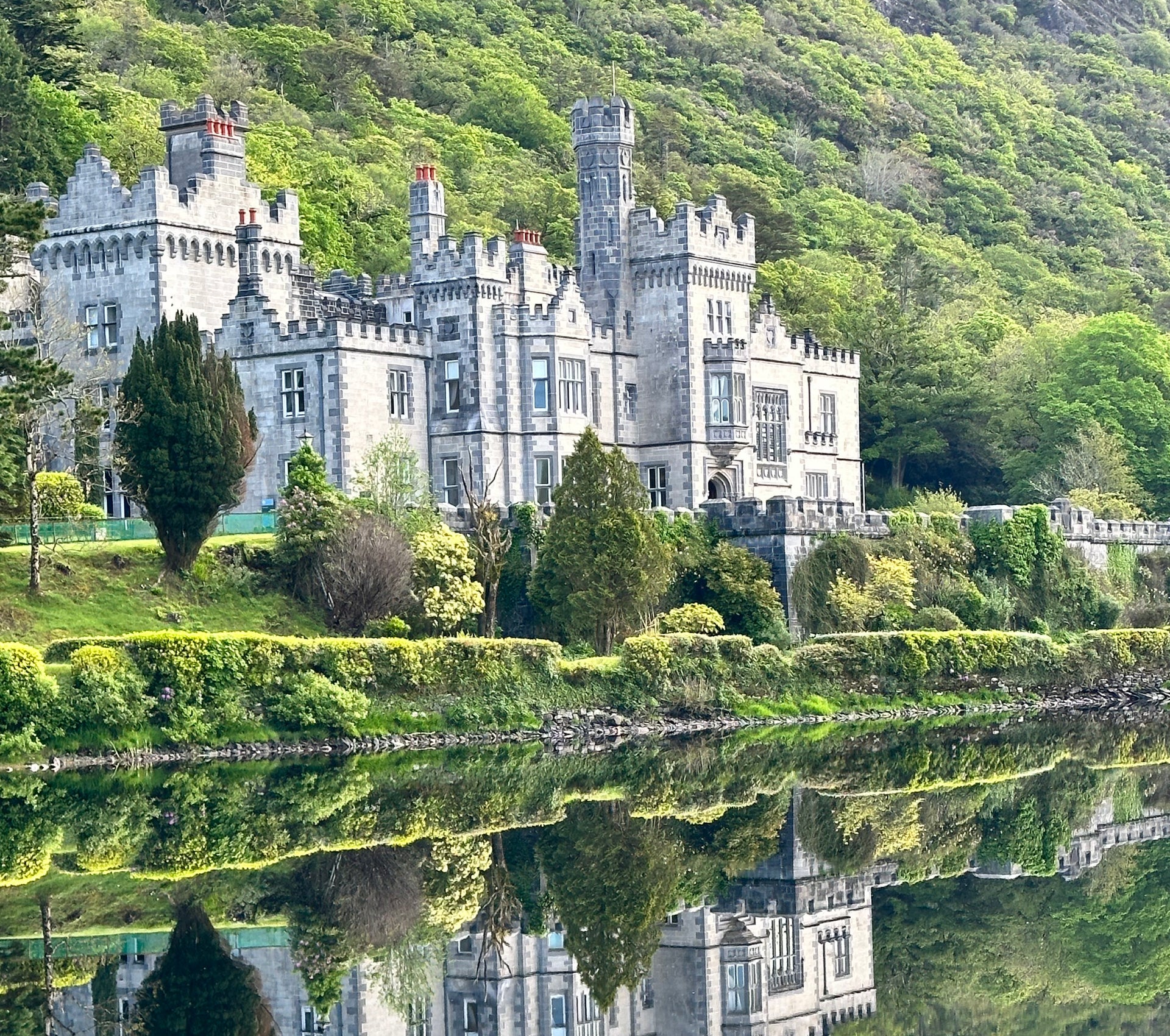Exterior of a large manor house overlooking a lake with a mountain in the background