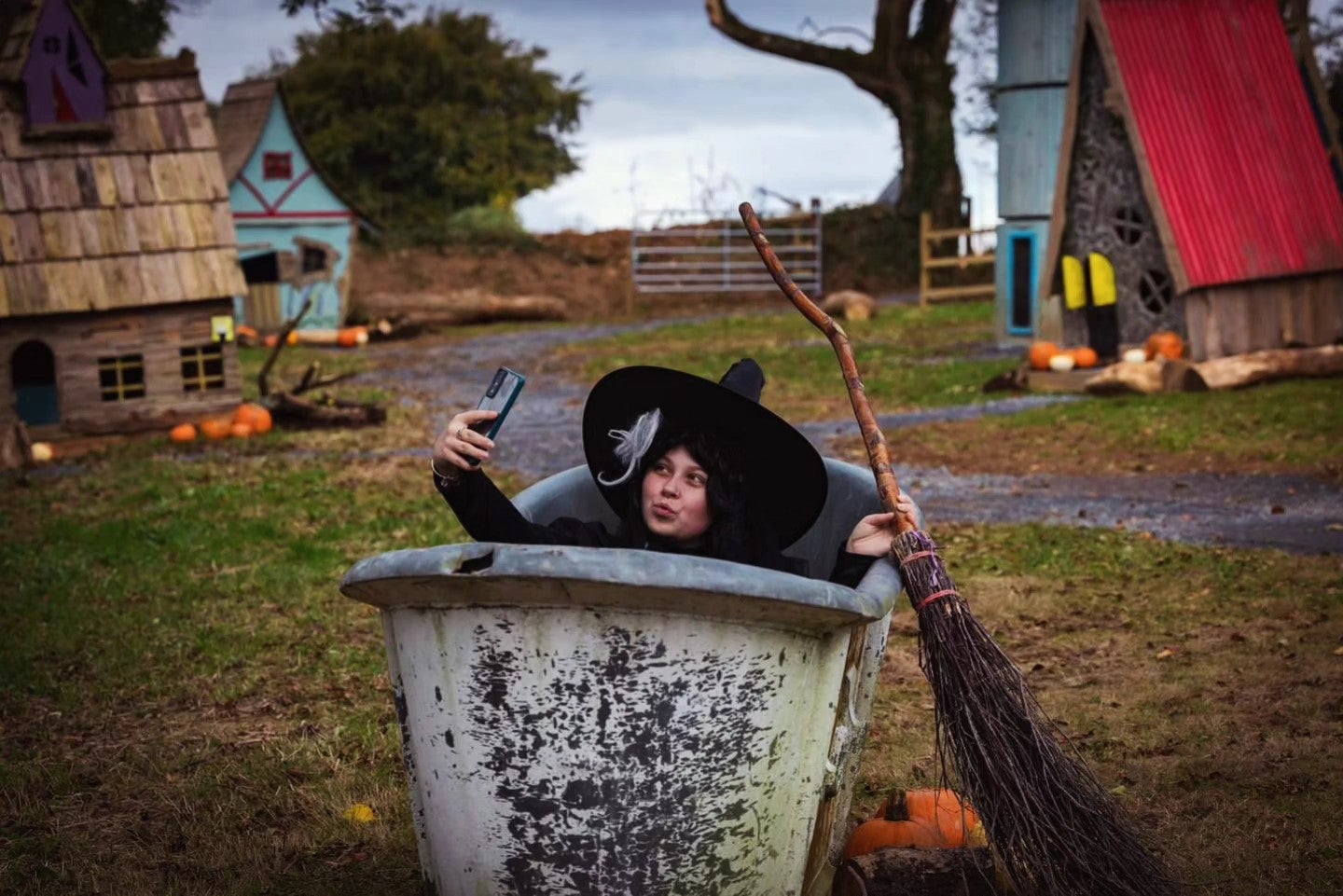 A person with large black hat and broom is in a large grey container taking a selfie.