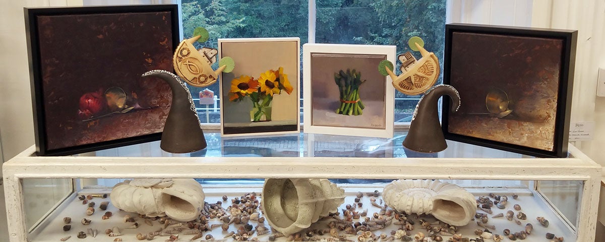 Four small paintings on top of a display case which has three large white sea shells
