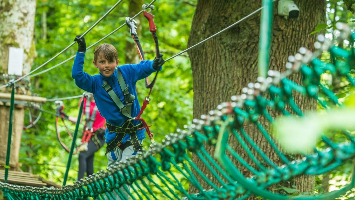 Boy walking across a rope bridge wearing a harness at Zipit Lough Key Ltd, Roscommon