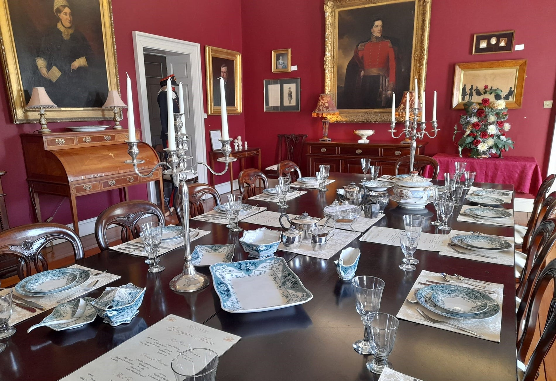 Large dining table set for service in a room with red walls and painting hanging on them