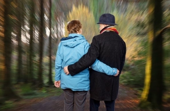 Aisteoirí an Bhaile Mhaigh Cuilinn Double Bill - 2 people viewed from behind with an arm around each other's waist with a blurry forest background.