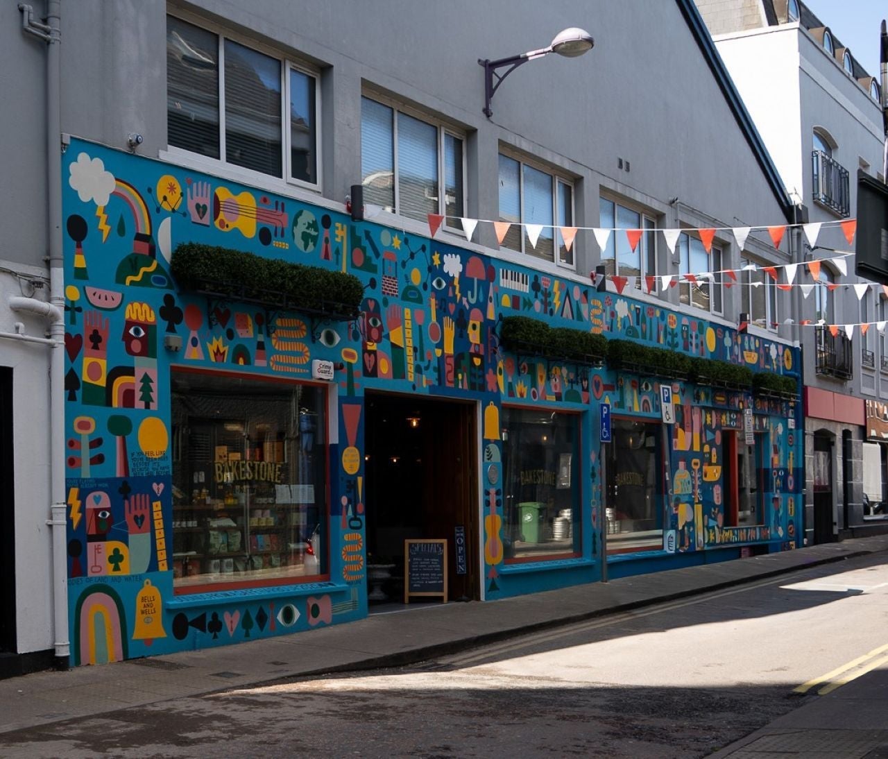 Outside a colourfully painted coffee shop on a street with red and white bunting