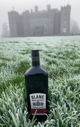 A bottle of whiskey on foggy dew grass with a castle in the background