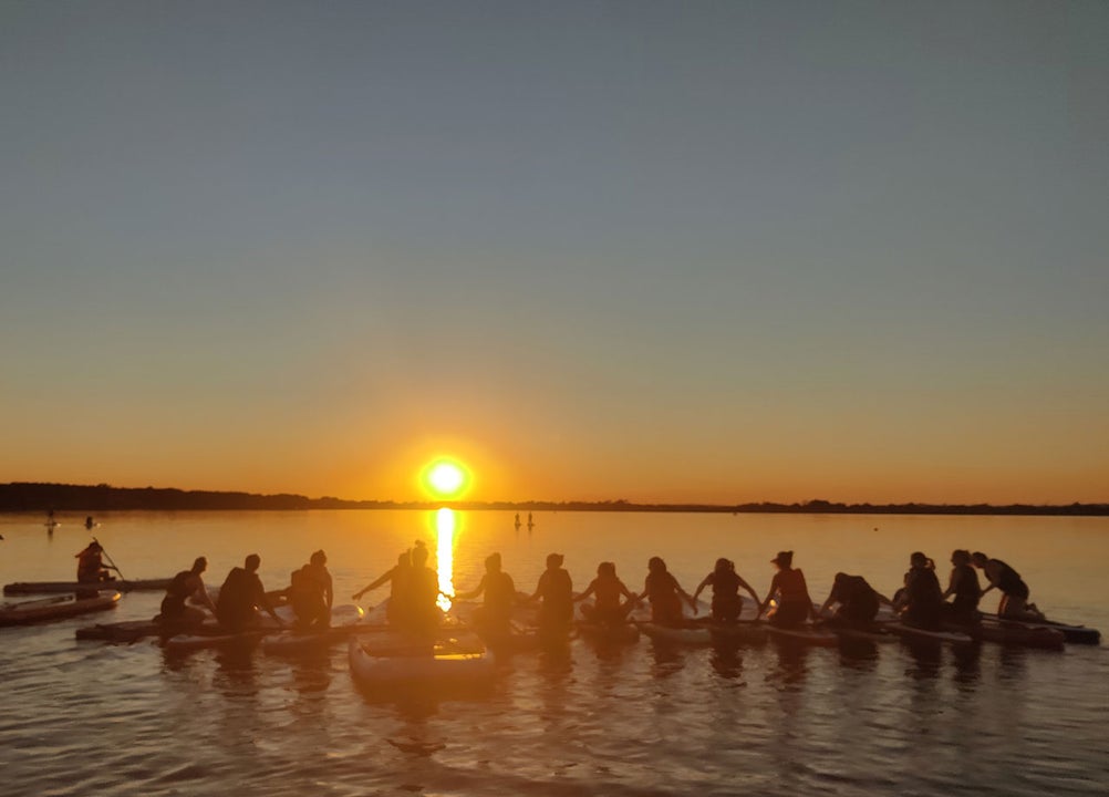 A group out on the paddleboard tour with the sun going down in the back ground