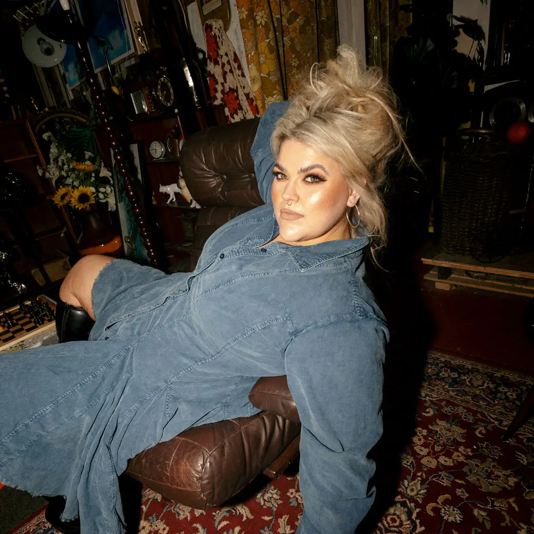 A woman in a blue denim dress is laying draped across a chair