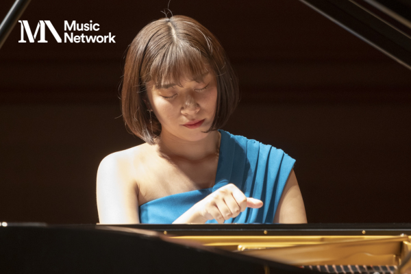 A woman seated at the keyboard of a piano looking down.