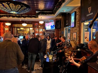 Interior of pub with a man playing guitar and a woman playing the banjo and people standing near bar counter