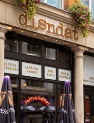 Outside a pub with a neon sign on the window and two unopened umbrellas