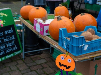 Pumpkins, coconuts and a handmade jack-o'-lantern decoration bring seasonal cheer to a farmers' market stall, alongside fresh local produce.