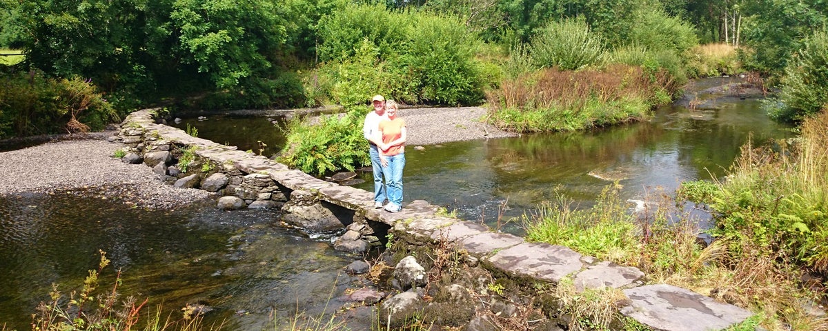 A couple standing on a small stone wall on a river