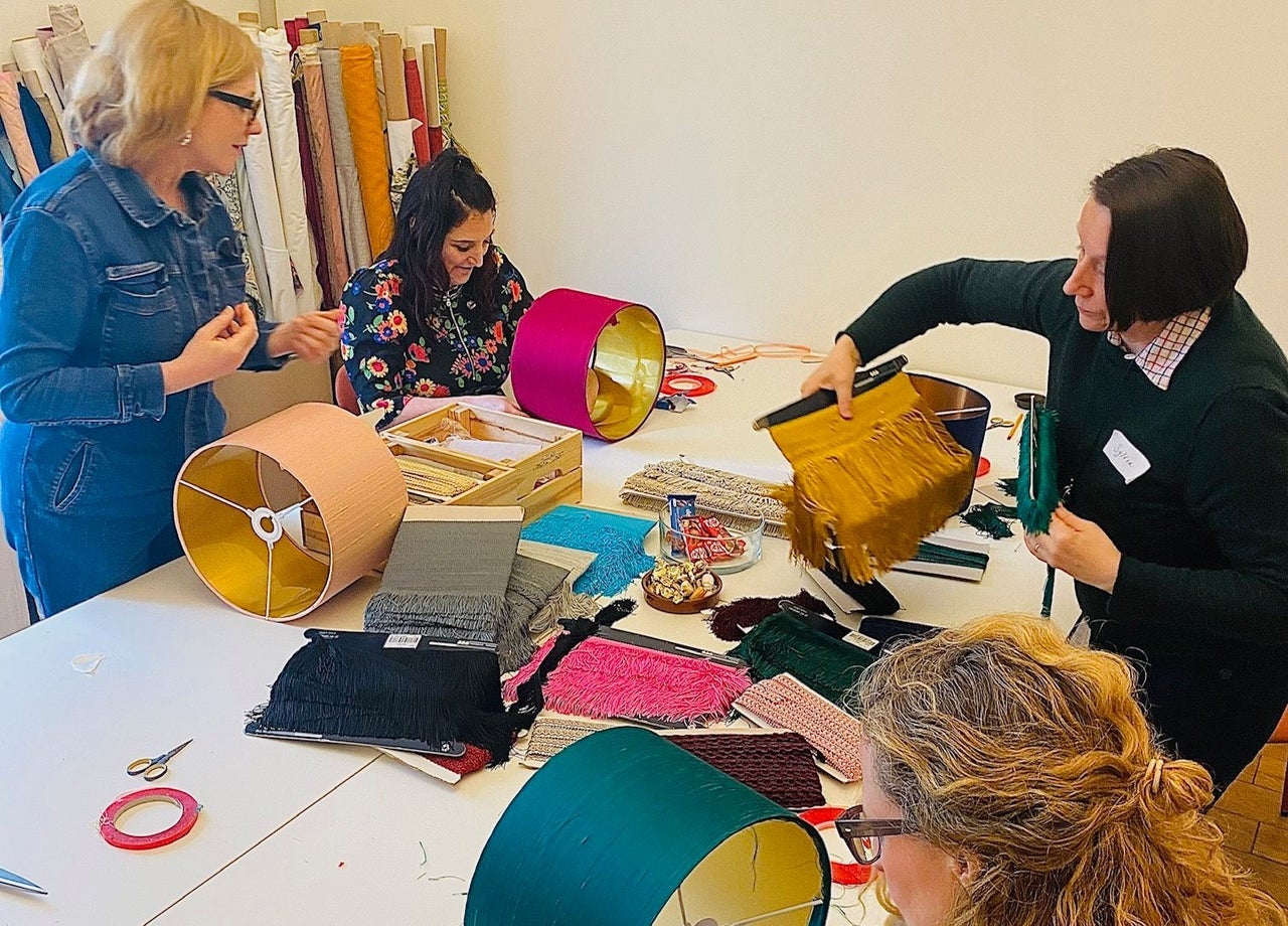 A group working at a table covered with fabrics and frames as they create lampshades during a workshop