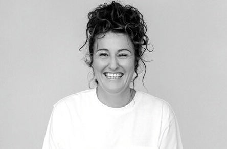 A broadly smiling woman with plain top and background.