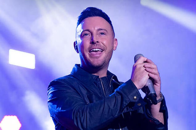 A smiling man holding a mic on a lit stage