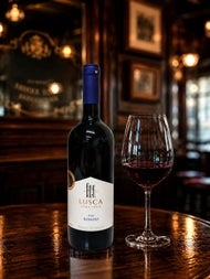 A bottle and glass of wine called Lusca on a dark wood coloured table top