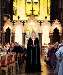 Person in medieval clothing standing between two tables in a banquet hall