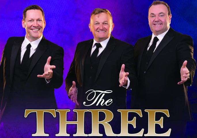 3 smiling men in dark suits and ties all with their left hands outstretched forwards.