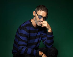 A man in sunglasses with one hand up to his mouth