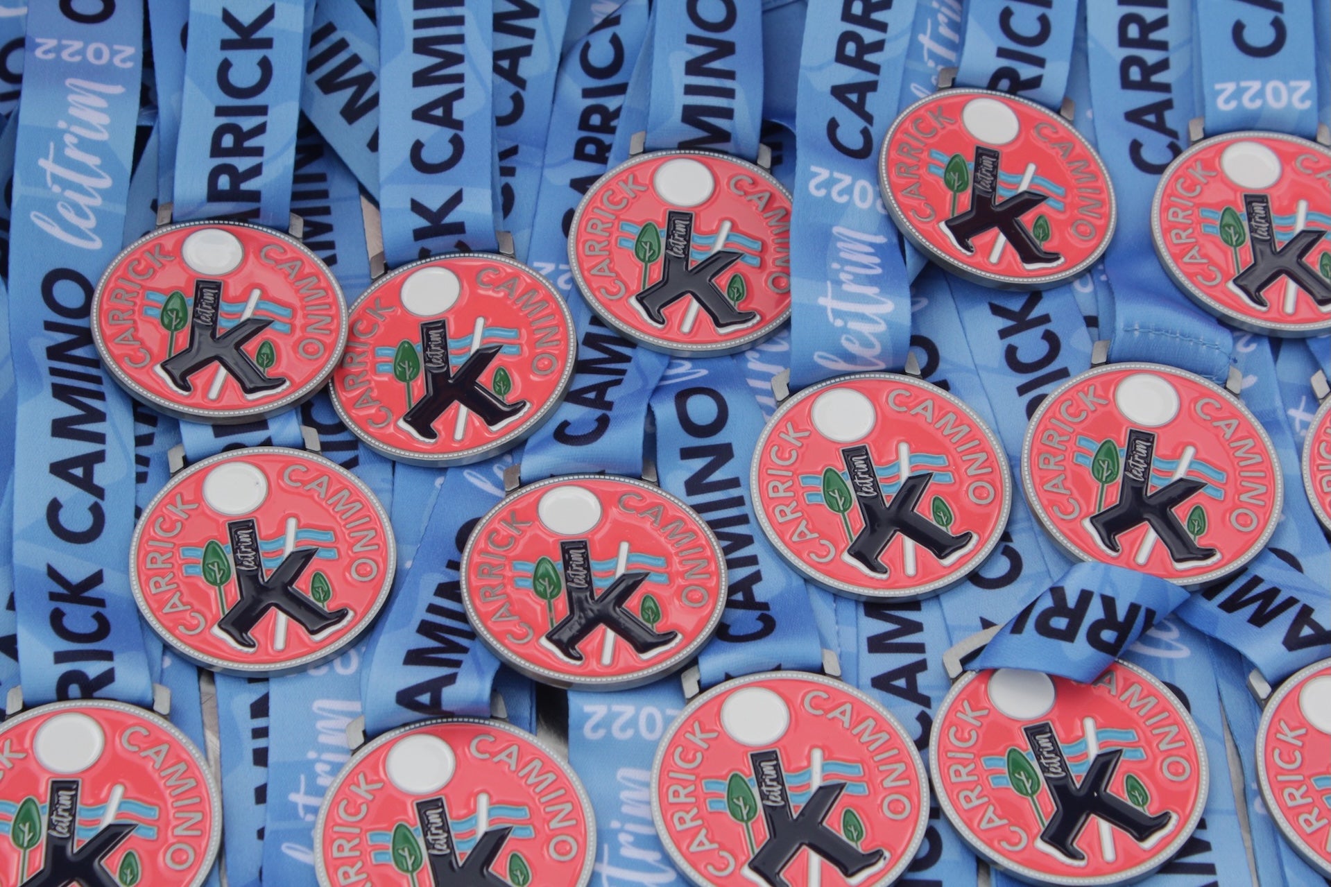 Lots of round red medals with logo for Carrick Camino on and blue ribbons