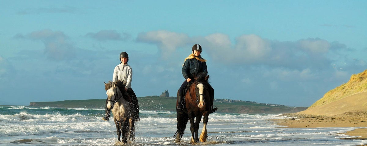 Two horse riders in the surf on the beach castle in the background
