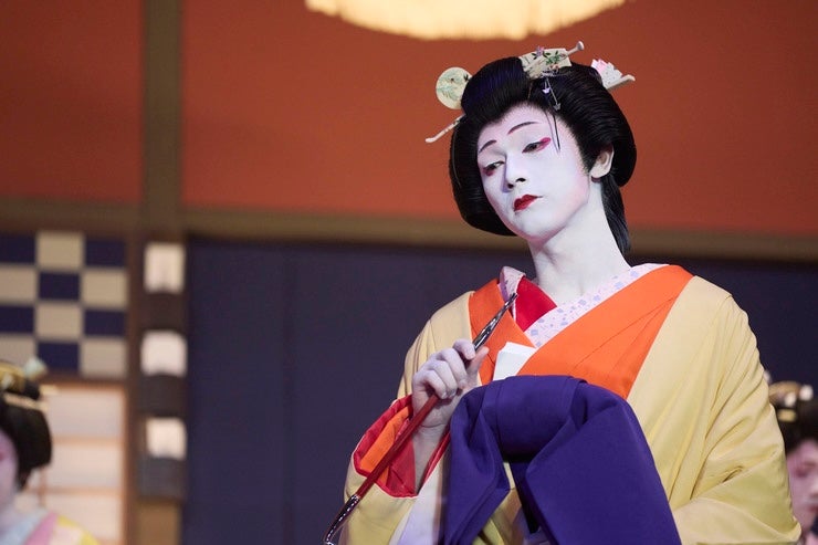 A sad person with very white painted face and black hair tied up in Japanese costume