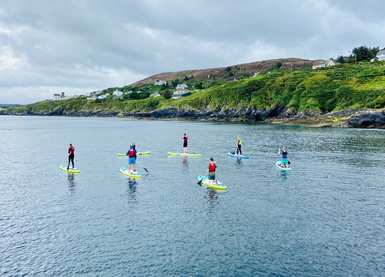 A group stand up paddle boarding along a craggy coastline
