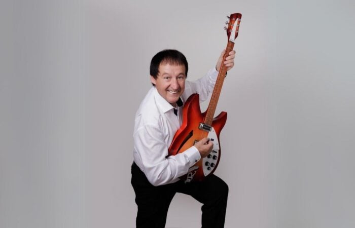 Declan Nerney live at Backstage Theatre Longford, a smiling man holding up a guitar vertically, resting on raised left knee.